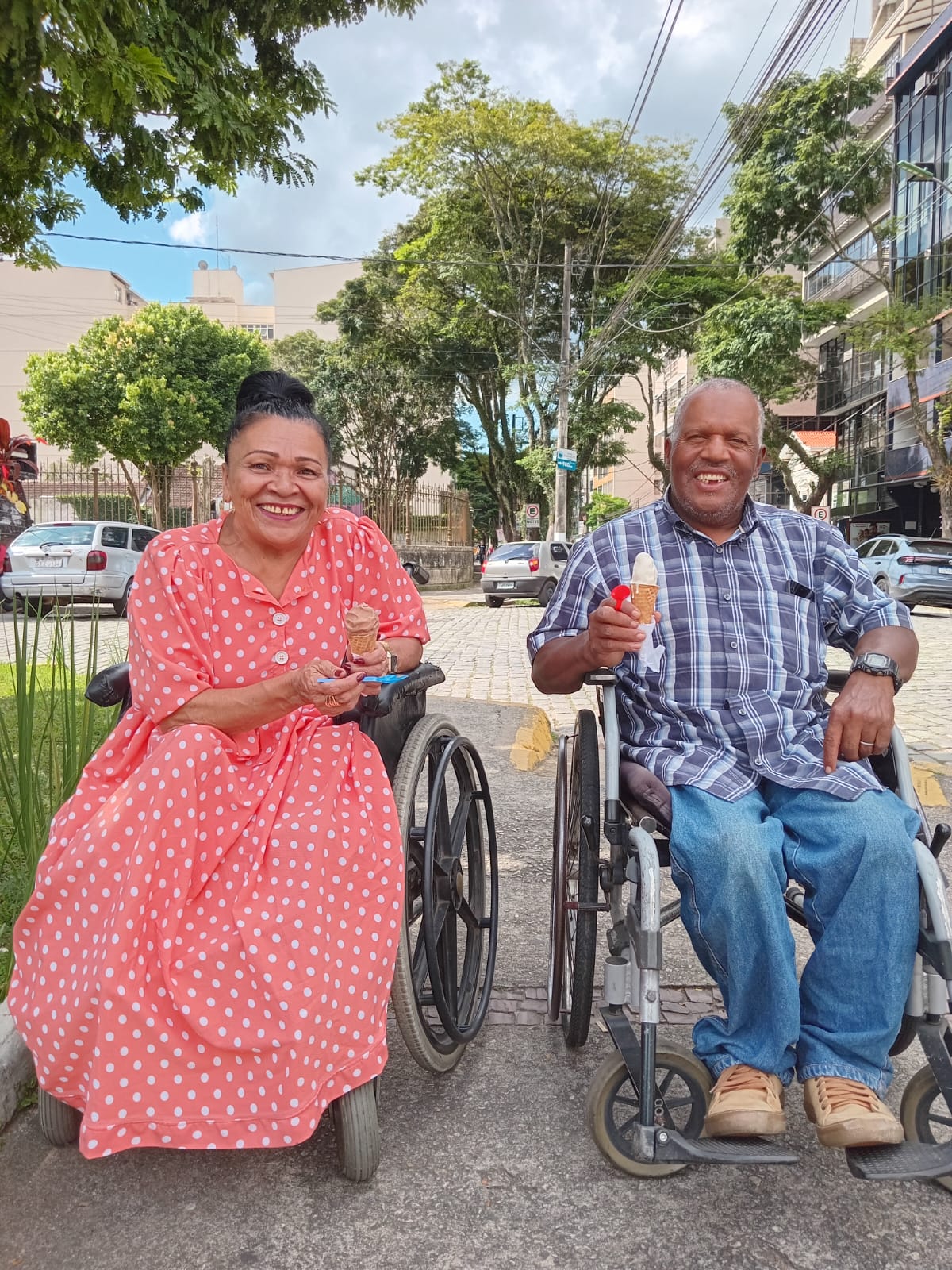 Lúcia e Marquinhos, casal apoiado pelo Grupo Borges, sorrindo em cadeiras de rodas com sorvetes